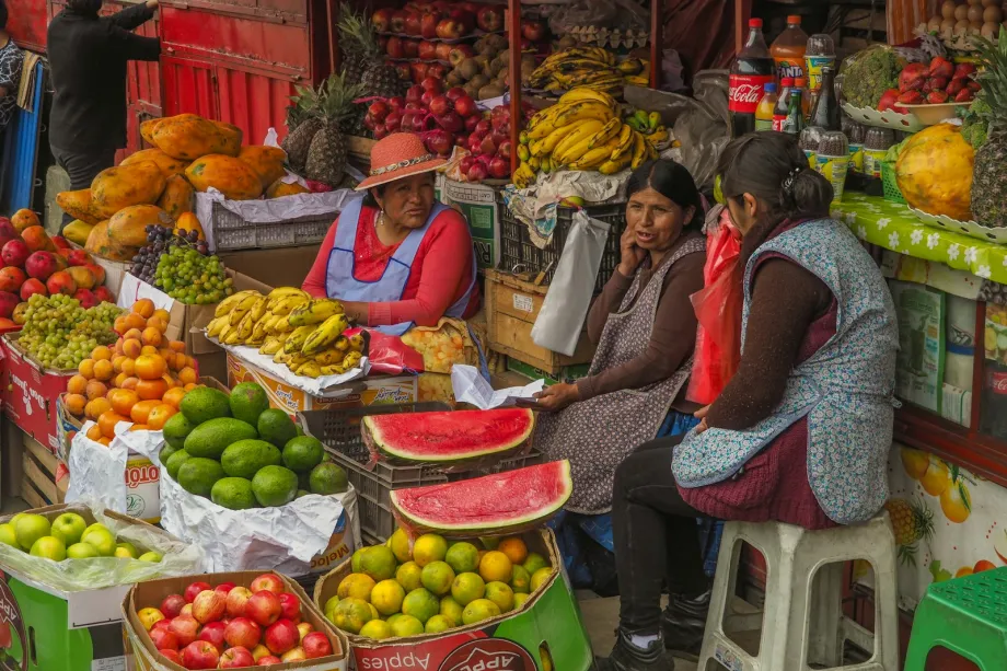 Three women sitting behind a sidewalk display of assorted fresh fruit