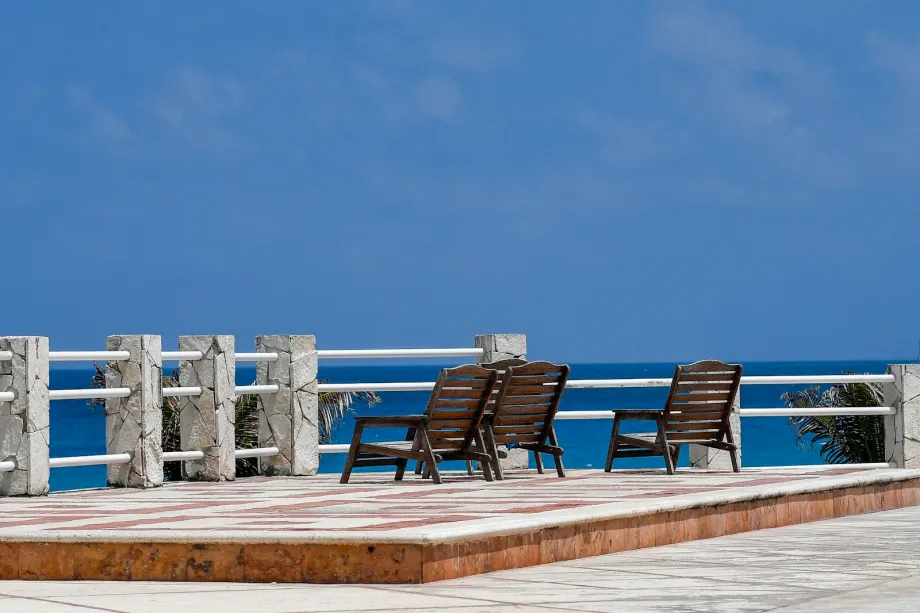 Two wooden lounge chairs on a terrace overlooking blue ocean